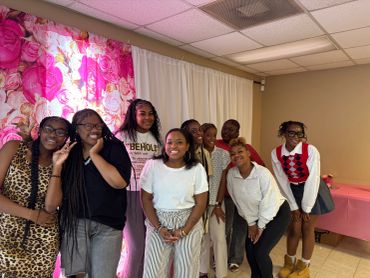 Group of smiling women posing indoors with pink floral backdrop.