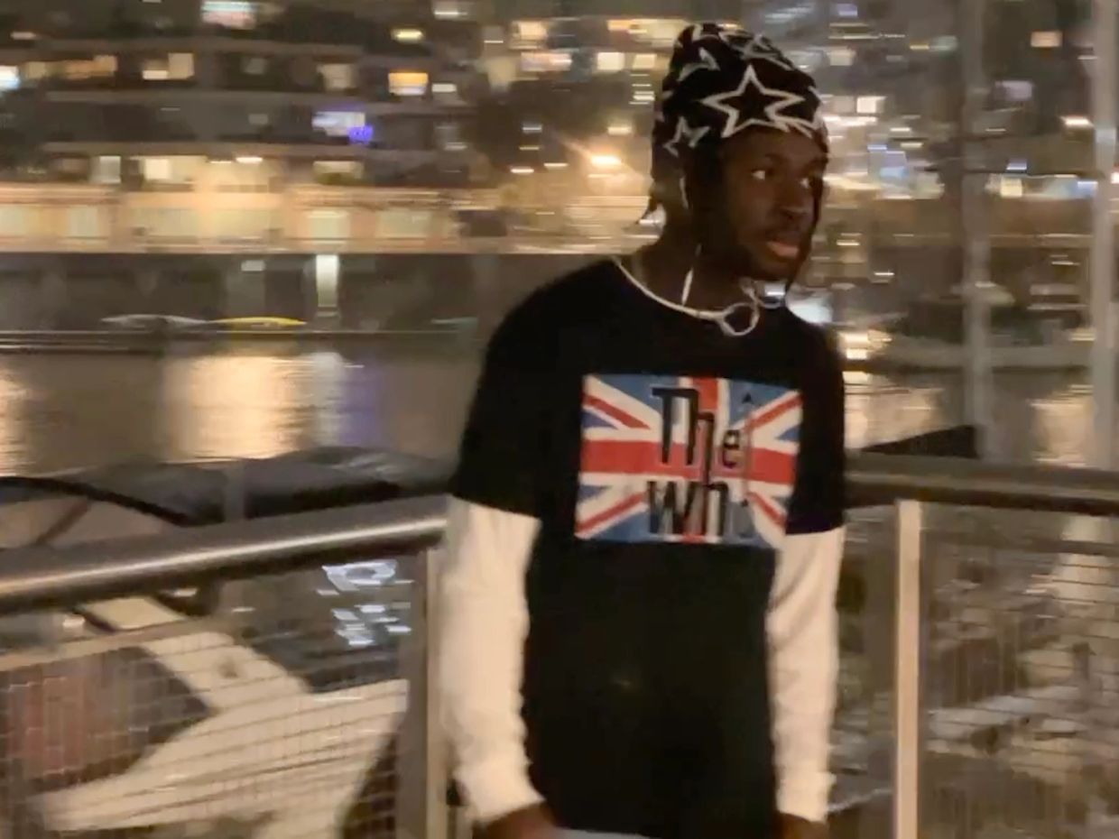 Man standing near waterfront at night wearing a black shirt with a British flag design.