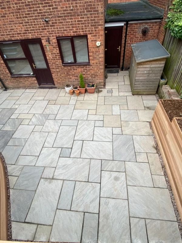 A clean, tiled backyard patio with a brick house and small wooden shed.