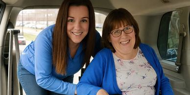 Two women smiling inside a vehicle, one seated and one leaning in.