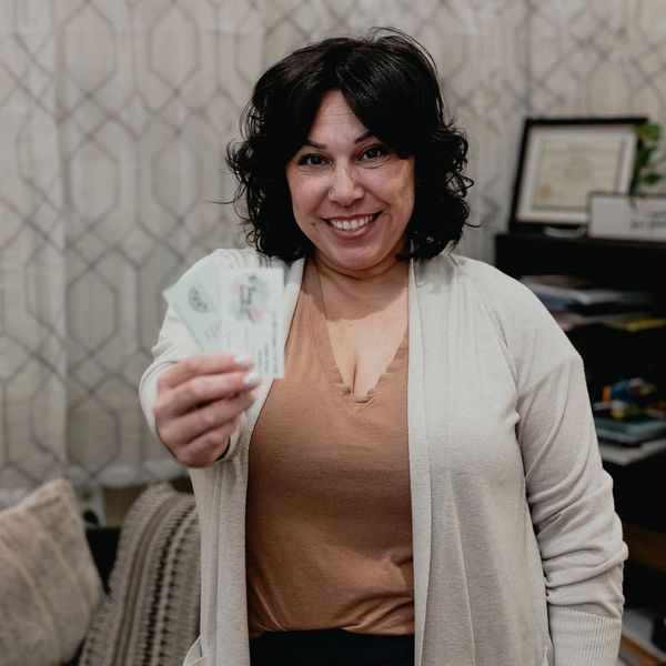 A smiling woman holding ID cards towards the camera.