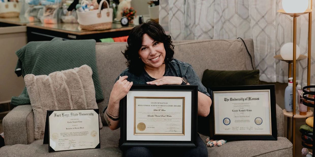 Woman proudly displays three framed certificates on a cozy couch.