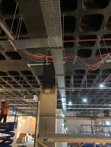 Construction site with exposed ceiling wiring and workers on lifts.