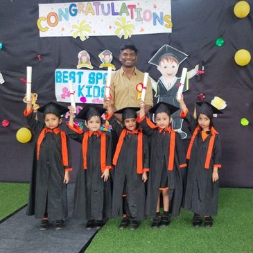 Kids in graduation gowns with a teacher celebrating.