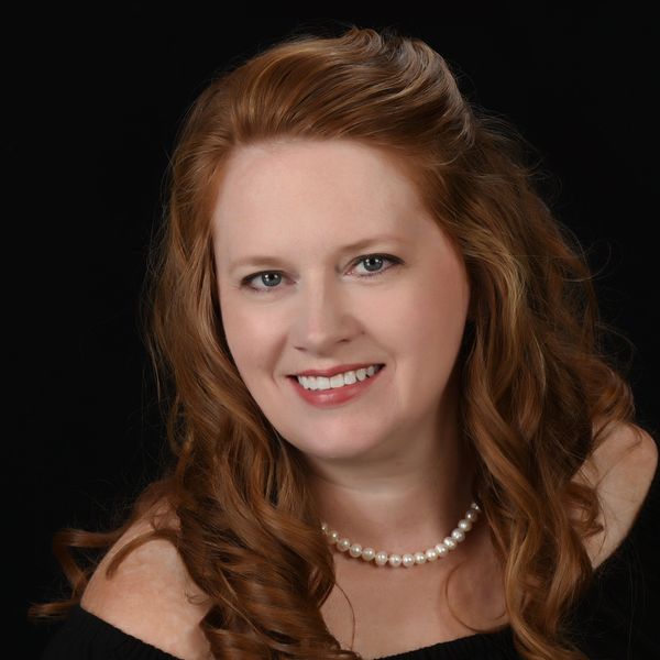 Smiling woman with red hair and pearl necklace.