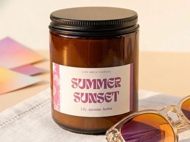 Amber jar soy wax candle labeled Summer Sunset with floral scents, next to sunglasses.