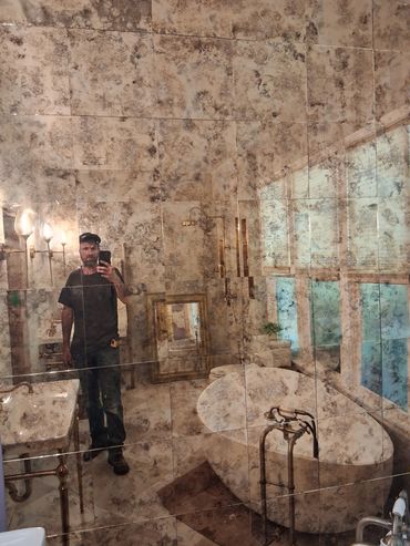 Man taking a selfie in a bathroom with marble walls and window reflection.