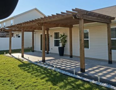 Wooden pergola over patio next to a house.