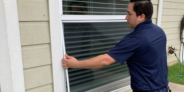 Technician inspecting a window screen for repair or replacement.