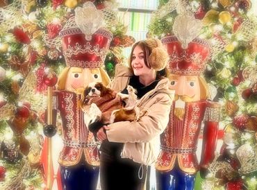 Girl standing in front of Christmas tree holding Cavalier King Charles Spaniel puppy