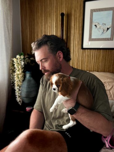 Man sitting indoors holding a small brown and white dog.