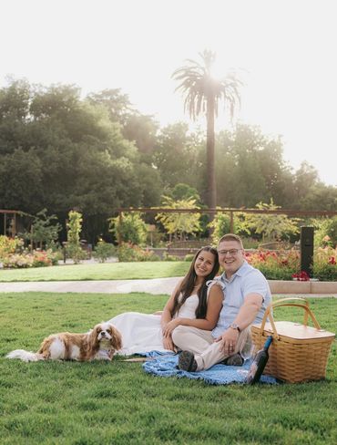 Man and woman sitting in grass with Cavalier King Charles dog