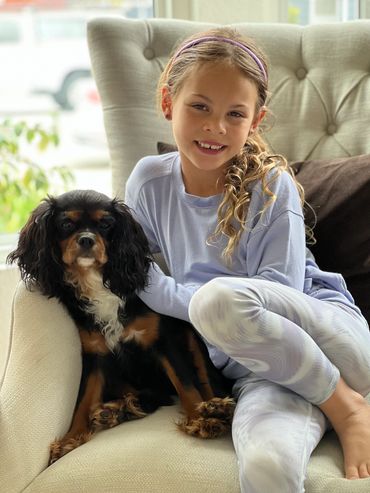 Young girl sitting on chair with black and tan Cavalier King Charles Spaniel dog