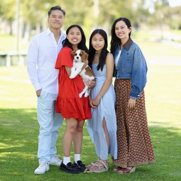 Family standing together with big smiles holding their Cavalier King Charles dog