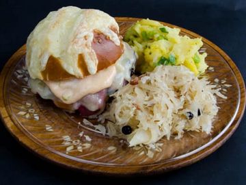 Reuben sandwich on a pretzel roll with cheese , german potato salad and sauerkraut.