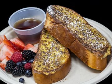 French toast with syrup and fresh berries on a white plate.