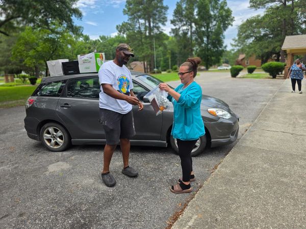 Two people exchanging items near a parked car loaded with boxes.
