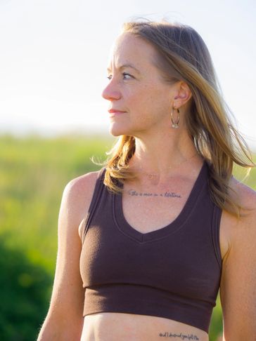 Woman looking to the side outdoors in a sleeveless top.