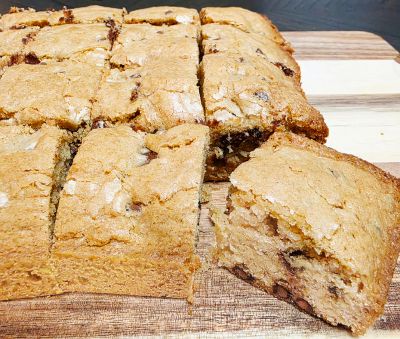Freshly baked chocolate chip cookie bars on a wooden board.