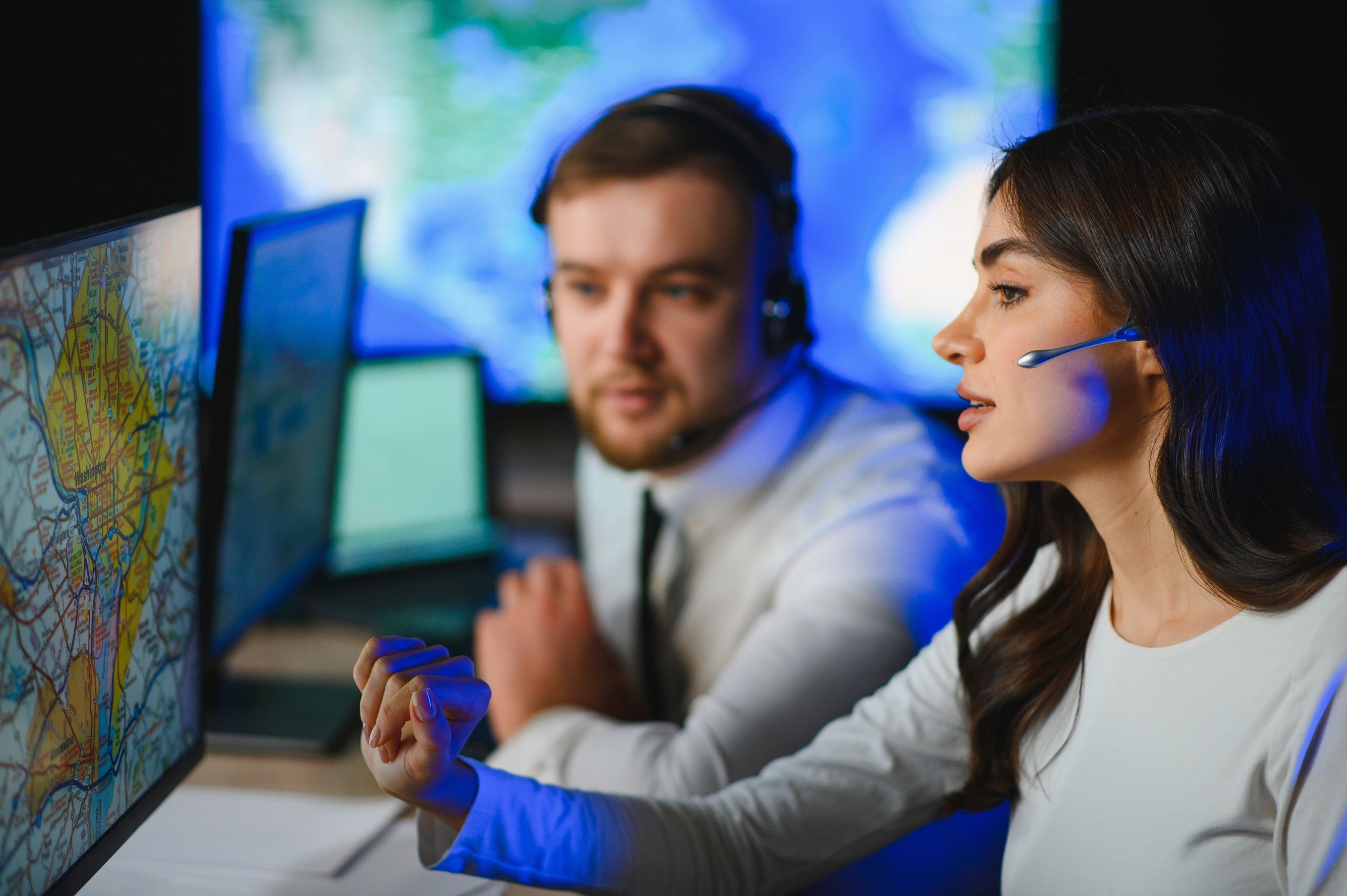 Two call center agents with headsets working at computer screens with maps.