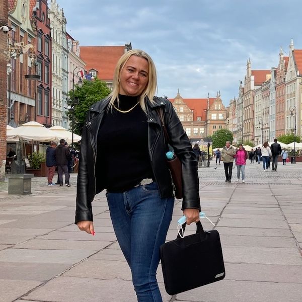A woman in a leather jacket posing on a city street with historic buildings.