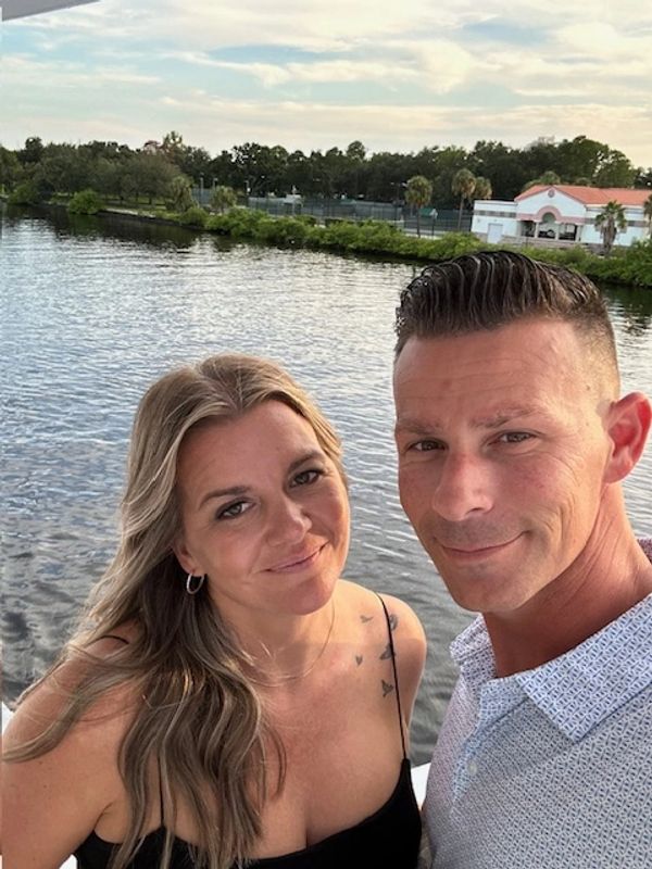 A smiling couple takes a selfie by a serene lakeside during sunset.