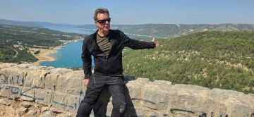 Man giving a thumbs up with ocean and hills in background.
