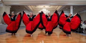 Five women dancing in traditional red and black dresses in a ballroom.