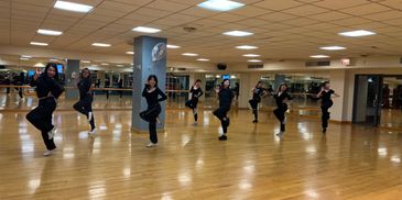 A group of women practicing dance poses in a studio with mirrors.
