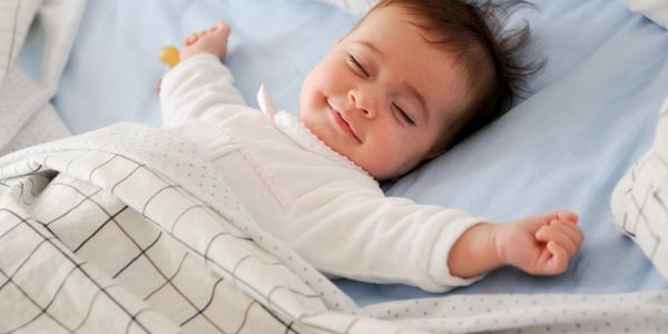Smiling baby peacefully sleeping with arms stretched out under a cozy blanket.