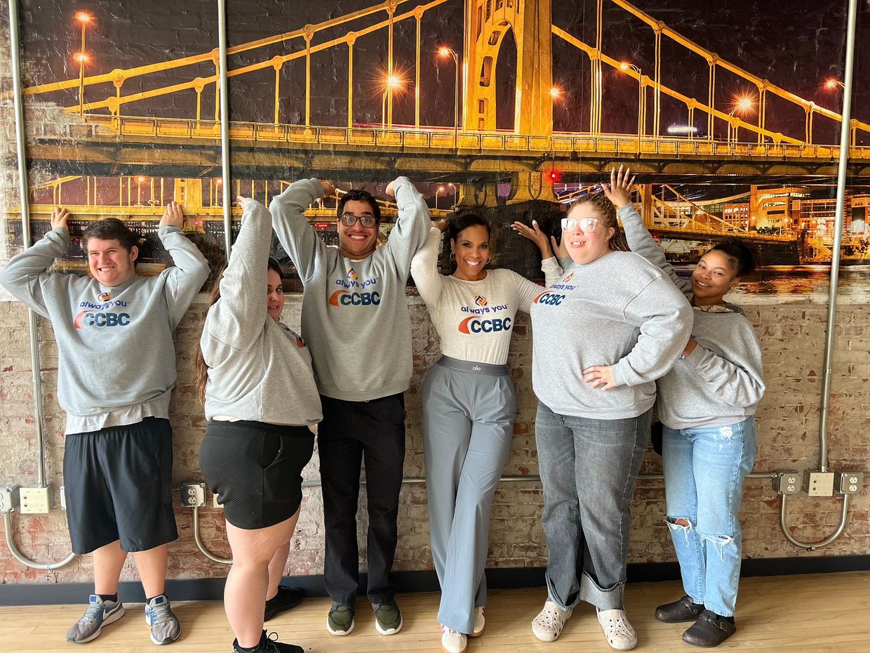 Group of six people smiling and posing in matching CCBC sweatshirts indoors.