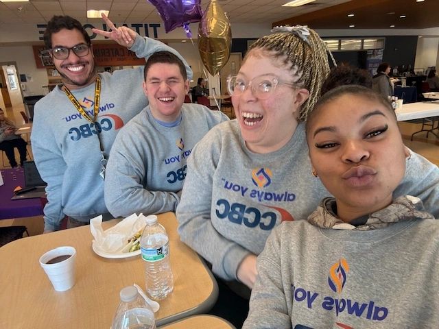 Four friends in matching sweatshirts smiling and posing for a selfie at a table.