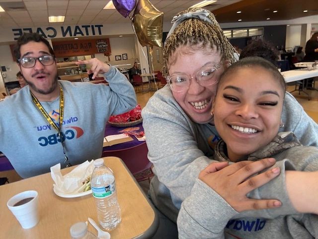 Three friends smiling and enjoying their time in a cafeteria with food and drinks on the table.