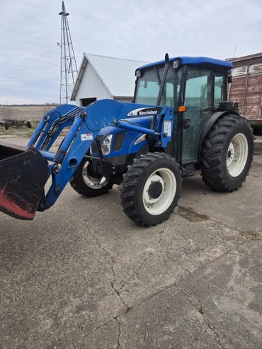Blue New Holland tractor with front loader on a farm driveway.