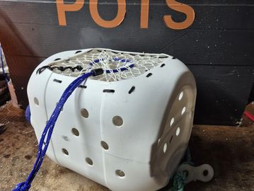 A weathered white trap with blue netting and rope.