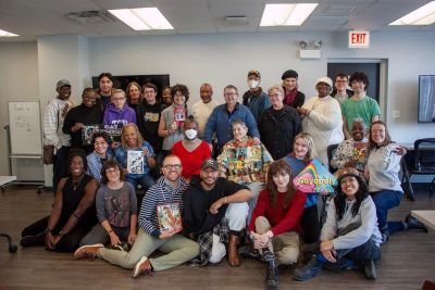 A diverse group poses together indoors, some holding colorful books and signs.