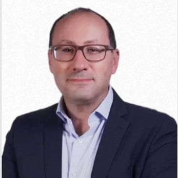 Man in a suit and glasses smiling.