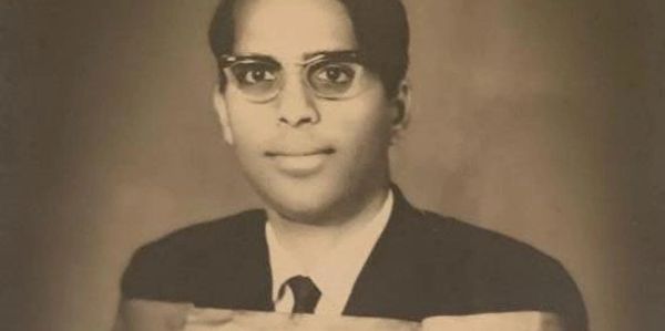 Black and white photo of a man in graduation attire holding a diploma.