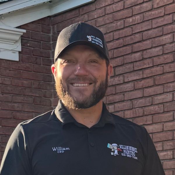 Smiling man in a black cap and shirt with a painting company logo.