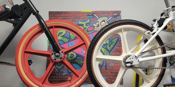 Two colorful bicycle wheels positioned side by side in front of graffiti art.