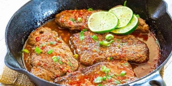 Spicy cooked meat garnished with sliced lime and green onions in a cast iron skillet.