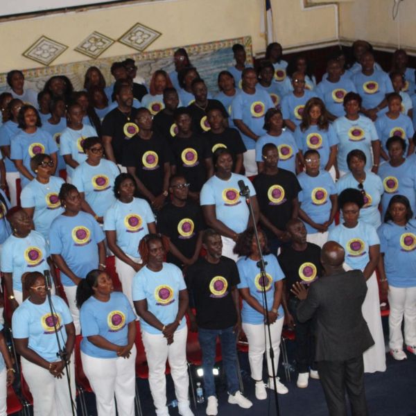 A choir group wearing matching blue and black shirts performing under a conductor.