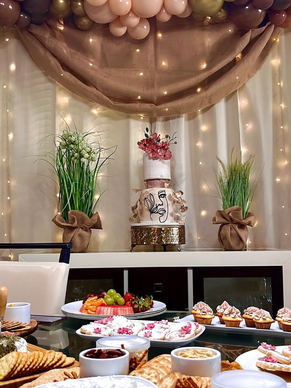 Elegant dessert table with artistic cake, cupcakes, and fresh fruits under balloon and light decoration.