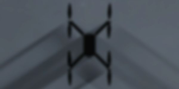 Silhouette of a drone in flight casting shadows on a gray background.