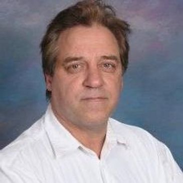 Portrait of a middle-aged man in a white shirt against a blue-gray background.