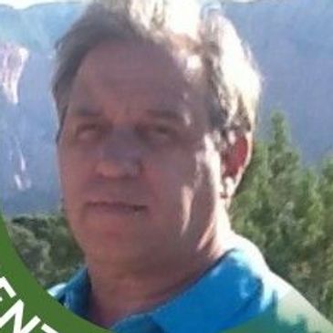 Man posing outdoors with mountains and trees in the background.