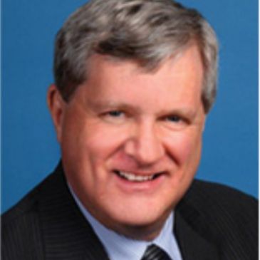 Portrait of a middle-aged man in a suit smiling against a blue background.