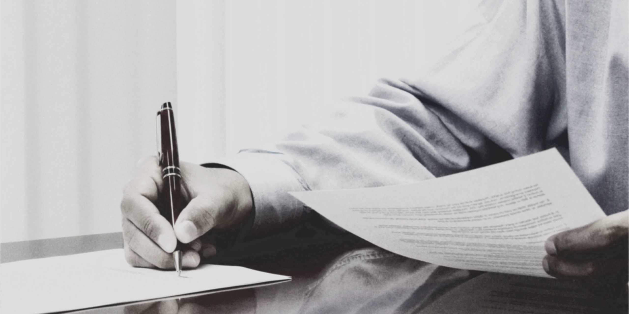 Person signing a document at a desk with a pen in hand.