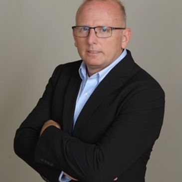 Professional man in glasses wearing a black suit with arms crossed.