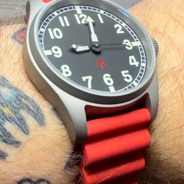 Close-up of a wristwatch with a red strap on a tattooed wrist.